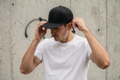 Homme ajustant la fermeture snapback d'une casquette noire structurée devant un mur en béton urbain