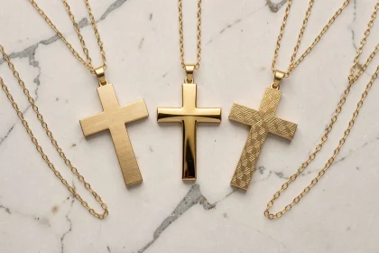 Trois pendentifs croix en or aux finitions différentes — mat, poli et gravé — sur marbre blanc, bijoux tendance 2026